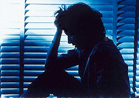 AFP6E1 Silhouette of a woman sitting by a window in a dim room and holding her head