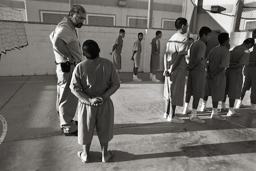 "Voices from Juvenile Detention: Kids Behind Bars" It sounds harmless: “pre-trial detention.” But the reality is far different. In a squat block building in Laredo, Texas—and in similar places around the nation—children await trial or placement in concrete cells while the underlying issues that led to their behavior fester. Some are addicts who need treatment; others are kids battling mental illnesses. Many are angry and have been virtually abandoned by absentee or irresponsible parents. Some spend a few days, others months, but despite the efforts of a small corps of dedicated professionals, few actually receive treatment for the issues that brought them to Juvenile. /// Inmates, ages 10-16, wait in line to march back to their cells in the exercise yard at the Webb County Juvenile Detention facility. This is the world of young felons, of kids gone astray, of children who cry for their mothers from behind bars. Some have skipped class too much, some have murdered in cold blood. At least half of the kids have been incarcerated before. And, if society's attempts at rehabilitation ultimately fail--or if the parent can't or simply won't do anything to turn around years of neglect and abuse--just a few more visits to juvenile detention will harden some of these kids into full-fledged adult criminals.